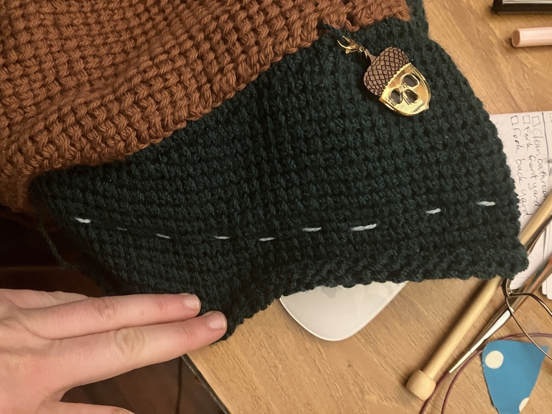 The body and partially constructed sleeve of a jumper worked in Tunisian crochet. The body is brown and the sleeve is dark green. The end of the sleeve has been sewn shut with a length of contrast yarn and large running stitches.